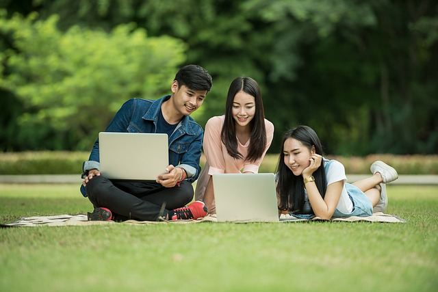Three students sitting on outdoor grass looking at laptop computers.